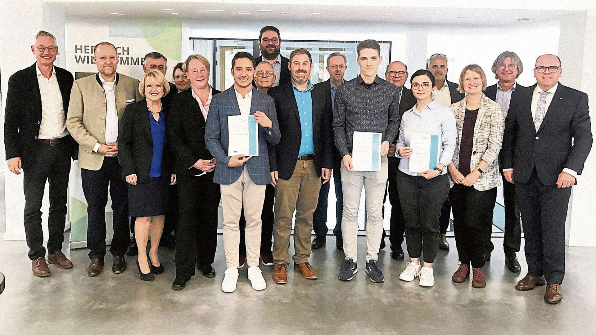 A group of 18 people, three of them presenting their certificates.